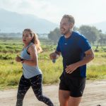 Two adults running on a rural dirt path, enjoying a sunny day outdoors.